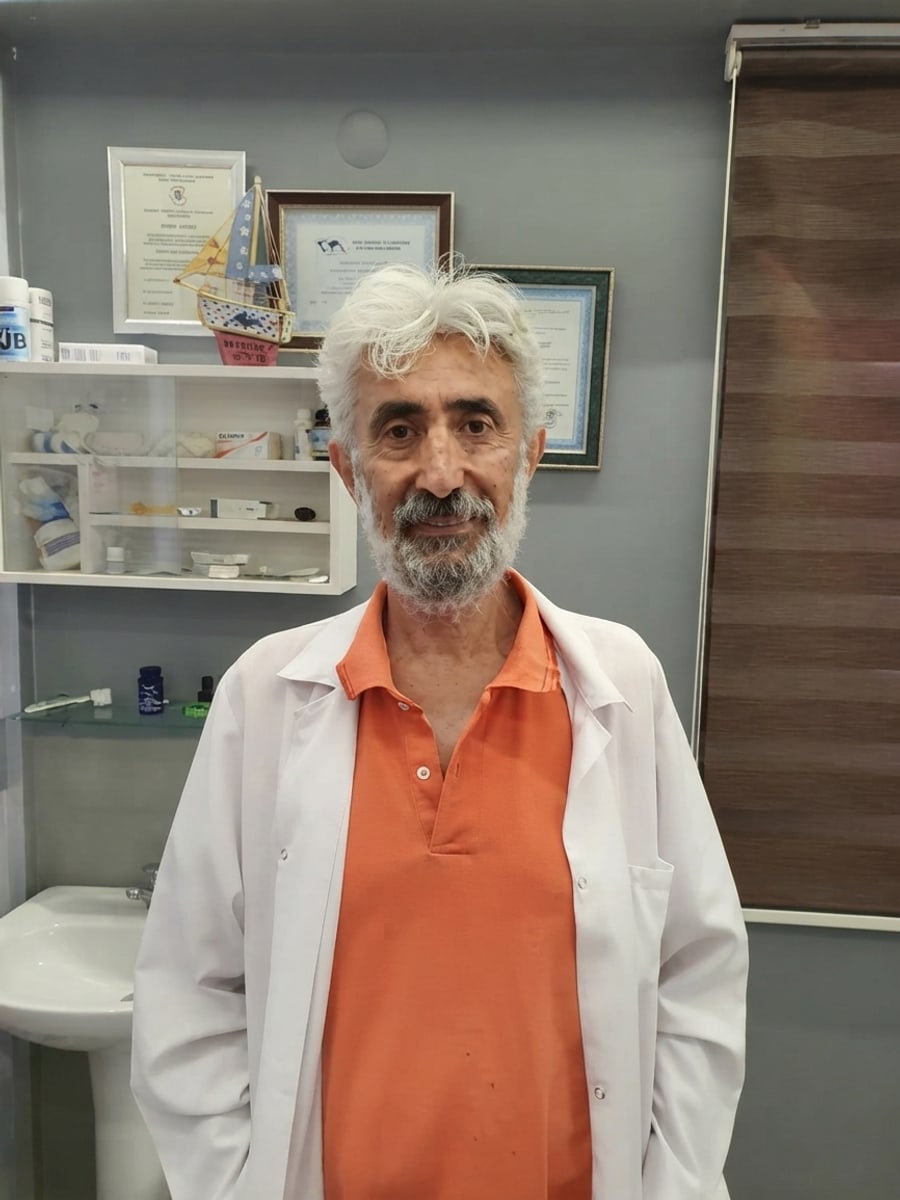 Yavuz Dinler kliniğinde, beyaz önlük ve turuncu polo tişörtle, arkasında sertifikaları